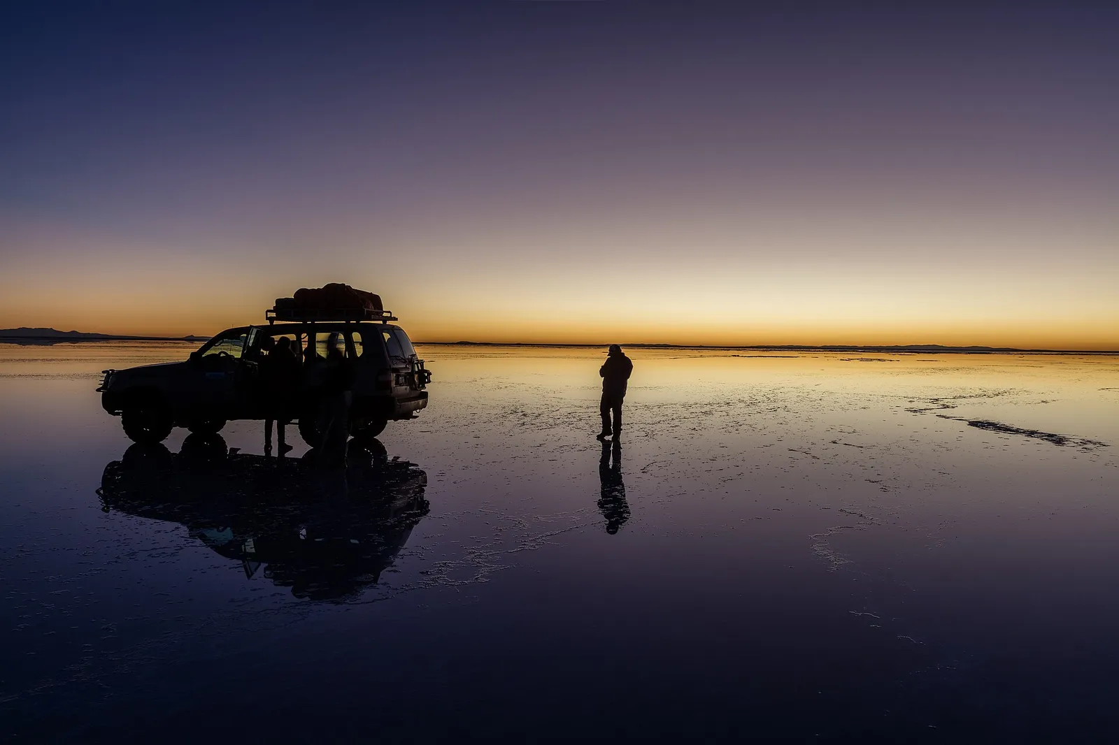 Amanecer en el Salar de Uyuni con un 4x4 reflejado en el agua